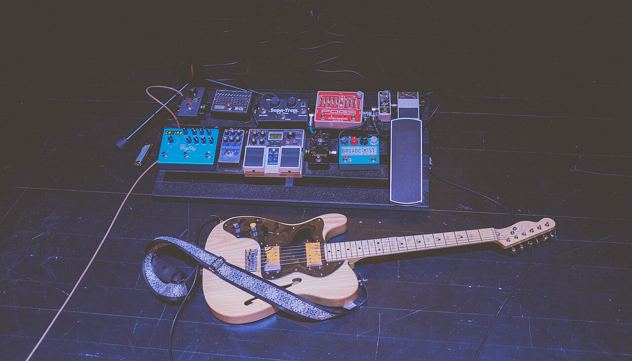 Guitarra eléctrica conectada a un pedalboard sobre un escenario de concierto