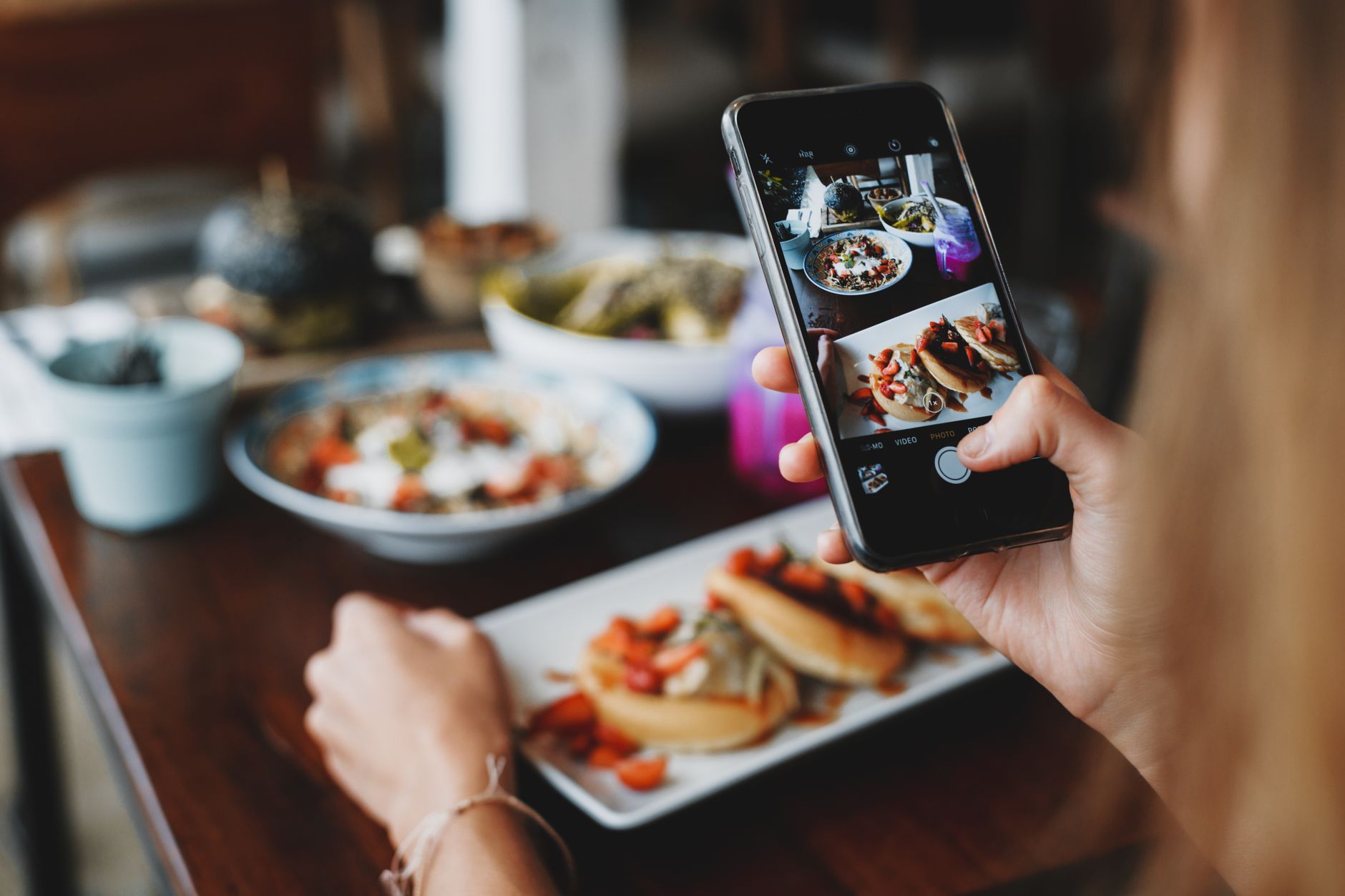Mujer fotografía varios platillos con su celular, imagen ilustrativa de las historias de Instagram donde se sugiere Higher de Creed